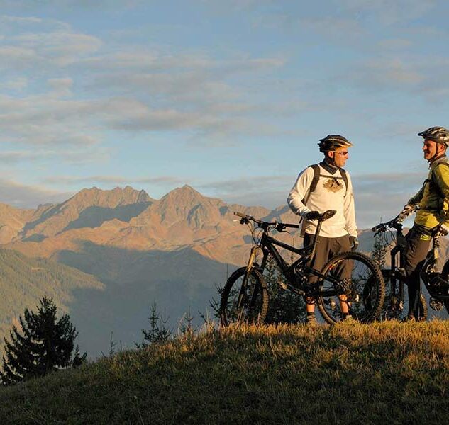 Zwei Männer stehen sich mit ihrem Fahrrad gegenüber und genießen den Blick auf die Alpen