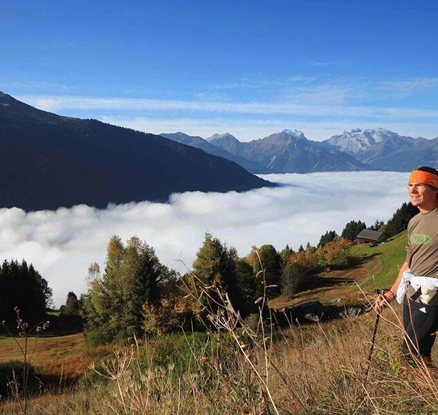 A man hikes up the mountain, the valley disappears under the clouds and he enjoys the view.