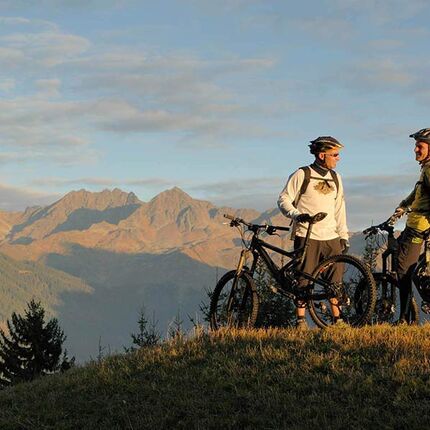 Zwei Männer stehen sich mit ihrem Fahrrad gegenüber und genießen den Blick auf die Alpen