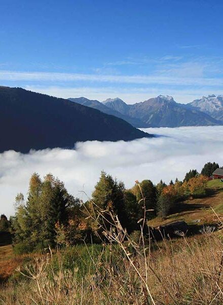 A man hikes up the mountain, the valley disappears under the clouds and he enjoys the view.