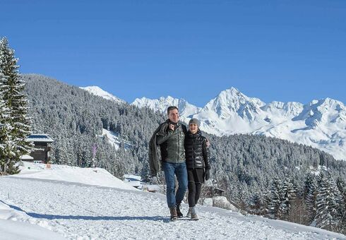 Ein Paar geht am Kristberg Wandern. Sie gehen Arm in Arm durch den Schnee und bestaunen das Winterpanorama.