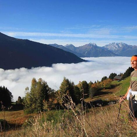 A man hikes up the mountain, the valley disappears under the clouds and he enjoys the view.