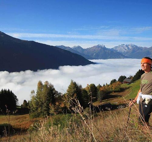 A man hikes up the mountain, the valley disappears under the clouds and he enjoys the view.