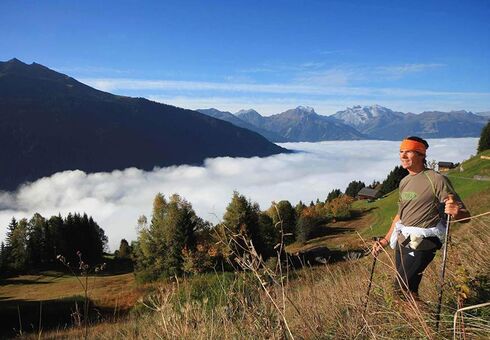 A man hikes up the mountain, the valley disappears under the clouds and he enjoys the view.