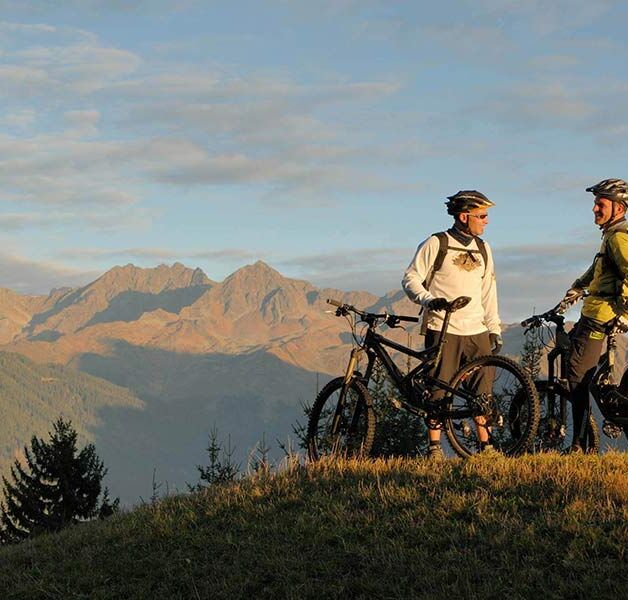 Two men face each other on their bicycles and enjoy the view of the Alps