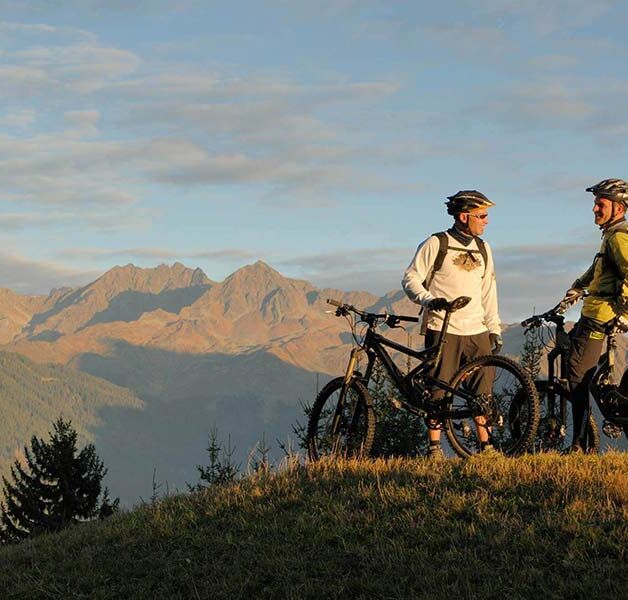 Zwei Männer stehen sich mit ihrem Fahrrad gegenüber und genießen den Blick auf die Alpen