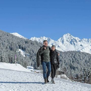 Ein Paar geht am Kristberg Wandern. Sie gehen Arm in Arm durch den Schnee und bestaunen das Winterpanorama.