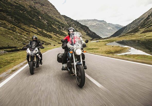 Two motorcyclists on the Silvretta High Alpine Road – a crystal-clear mountain lake in the foreground and the majestic peaks of the Silvretta mountains in the Austrian Alps in the background.
